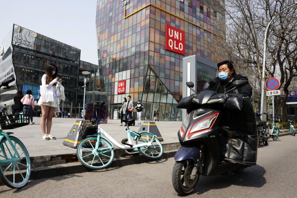 A man wearing a mask rides past a Uniqlo store in Beijing on Thursday, March 25, 2021. China's ruling Communist Party is lashing out at H&M and other clothing and footwear brands as it retaliates for Western sanctions imposed on Chinese officials accused of human rights abuses in the northwestern region of Xinjiang. (AP Photo/Ng Han Guan)