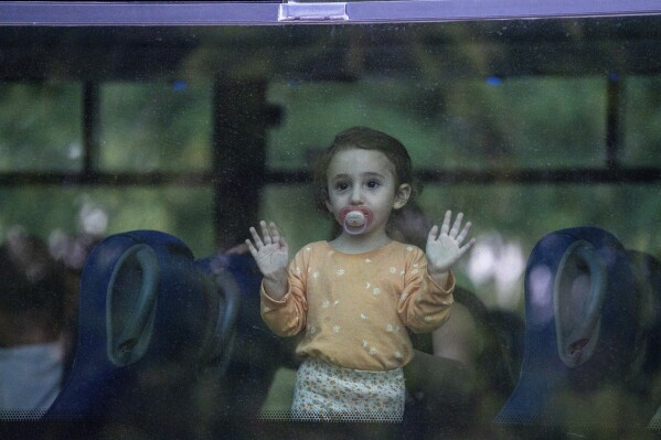 A young girl looks through a bus window as her family departs the northern Israeli city of Kiryat Shmona, Israel, Friday, Oct. 20, 2023. The Israeli military announced Friday it would evacuate the border city a day after three residents were injured by cross-border fire from militants in Lebanon. (AP Photo/Baz Ratner)
