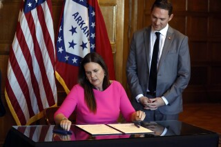 FILE - Arkansas Gov. Sarah Huckabee Sanders signs a bill requiring age verification before creating a new social media account as Sen. Tyler Dees, R-Siloam Springs, looks on during a signing ceremony, Wednesday, April 12, 2023, at the state Capitol in Little Rock, Ark. , NetChoice, a tech industry trade group, is suing Arkansas over its law requiring parental permission for minors to create new social media accounts. (Thomas Metthe/Arkansas Democrat-Gazette via AP)