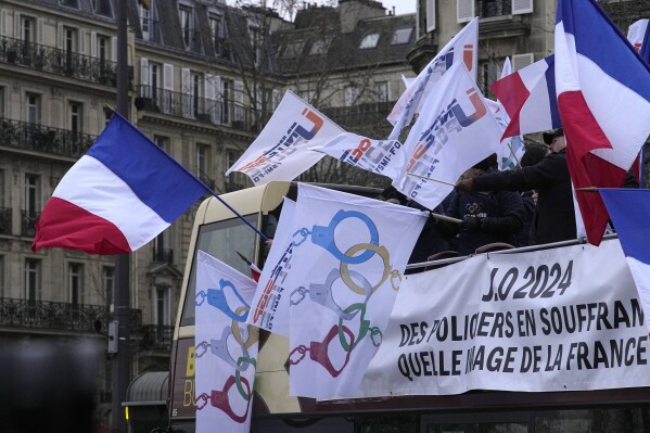 Police officers demonstrate with flags turning the olympic rings as handcuffs during a demonstration Wednesday, Jan. 10, 2024 in Paris. Police officers held a protest action in Paris as police unions said officers who will be working during the Paris Olympics have no guarantee that they'll be able to take vacation during summer and get a compensation package. A massive security operation is planned for the Games, with tens of thousands of police and soldiers deployed. (AP Photo/Michel Euler)