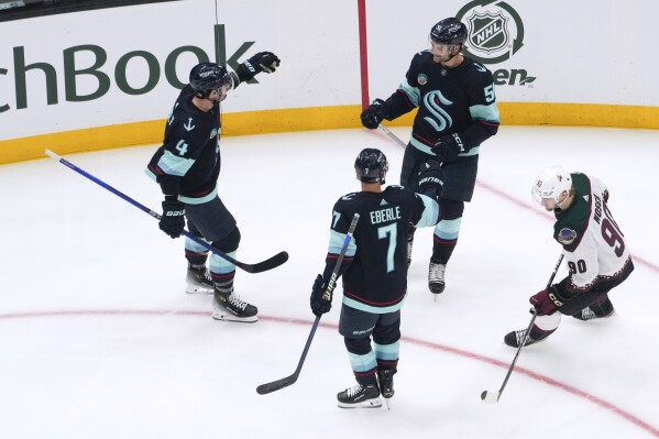 Seattle Kraken center Shane Wright, top right, celebrates his goal with Justin Schultz (4) and Jordan Eberle (7) as Arizona Coyotes defenseman J.J. Moser, right, skates away during the first period of an NHL hockey game Tuesday, April 9, 2024, in Seattle. (AP Photo/Lindsey Wasson)