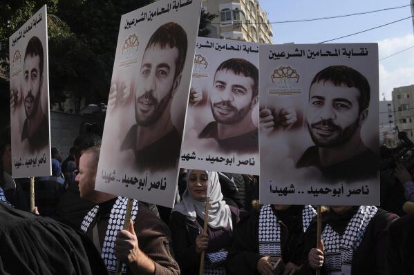 Palestinians hold posters of Palestinian prisoner Nasser Abu Hamid during a protest in front of the International Committee of the Red Cross office, Tuesday, Dec. 20, 2022, in Gaza City, after he died of lung cancer in Israel. Abu Hamid was a former leader of the Al Aqsa Martyrs' Brigade, the armed wing of Palestinian President Mahmoud Abbas's Fatah party. He had been serving seven life sentences after being convicted in 2002 for involvement in the deaths of seven Israelis during the second Palestinian intifada, or uprising, against Israel's occupation in the early 2000s. Arabic reads: " Nasser Abu Hamid is a martyr". (AP Photo/Adel Hana)