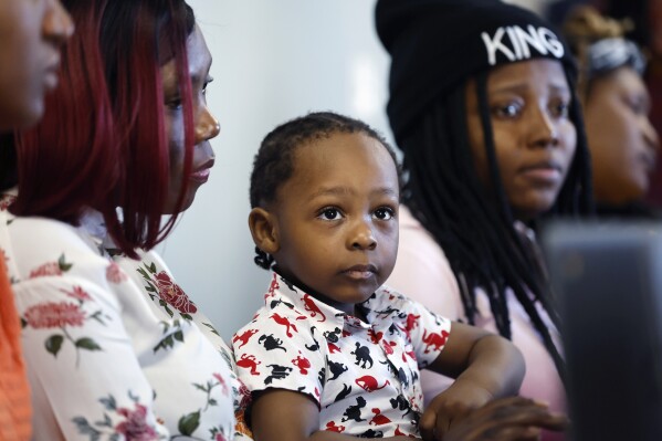 Micheline Jean Louis, left, holds her son Andy Jean Louis Louidor, center, while learning computer skills, Friday, Dec. 22, 2023, in a rectory building where they are staying at the Bethel AME Church in the Jamaica Plain neighborhood of Boston. Demand for has increased as Massachusetts struggles to find newly arriving migrants places to stay after hitting a state-imposed limit of 7,500 families in its emergency homeless shelter system last month. (AP Photo/Michael Dwyer)