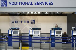 FILE - In this Oct. 14, 2020 file photo, United Airlines employees work at ticket counters in Terminal 1 at O'Hare International Airport in Chicago.  United Airlines will pay more than $49 million to settle criminal and civil accusations of defrauding the post office in the handling of international mail. The Justice Department said Friday, Oct. 26, 2021, that former employees of United’s cargo division falsified parcel delivery information for several years.  (AP Photo/Nam Y. Huh, File)