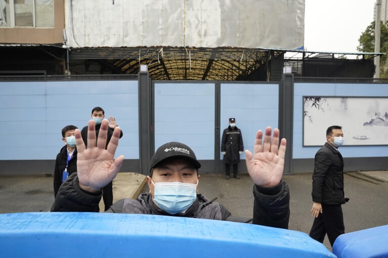 FILE - A security guard waves for journalists to clear the road after a convoy carrying the World Health Organization team entered the Huanan Seafood Market on the third day of a field visit in Wuhan in central China's Hubei province on Jan. 31, 2021. The hunt for COVID-19 origins has gone dark in China. An AP investigation drawing on thousands of pages of undisclosed emails and documents and dozens of interviews found feuding officials and fear of blame ended meaningful Chinese and international efforts to trace the virus almost as soon as they began, despite years of public statements to the contrary. (AP Photo/Ng Han Guan, File)