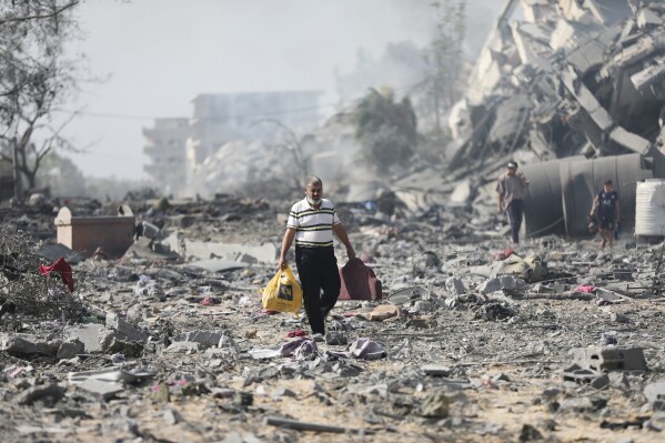 Palestinians walk by buildings destroyed in the Israeli bombardment on al-Zahra, on the outskirts of Gaza City, Friday, Oct. 20, 2023. (AP Photo/Ali Mahmoud)
