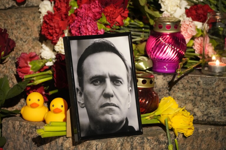 Un portrait du chef de l'opposition russe Alexei Navalny, des fleurs et des bougies sont déposées sur le sol alors que les gens se rassemblent pour rendre un dernier hommage à Alexei Navalny lors d'un mémorial aux victimes de la répression politique à Saint-Pétersbourg, en Russie, le vendredi 16 février 2024. .  (Photo AP/Dmitri Lavtski)