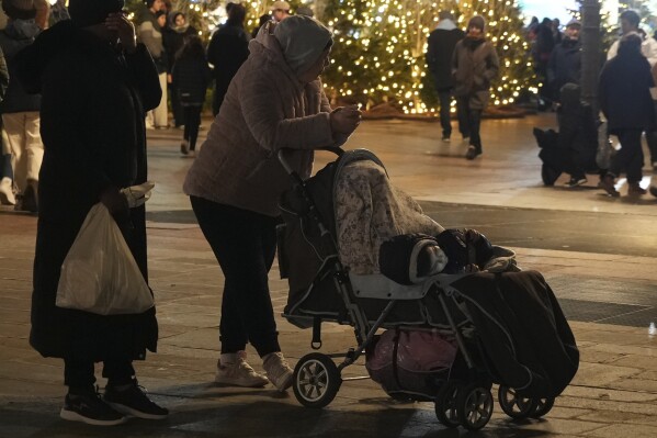 Migrants wait on the City Hall plaza in Paris, Monday Dec.25, 2023 as migrant families meet on Christmas Day seeking somewhere to stay. About 50 families with children between three months and 10 years old gathered on City Hall plaza on Christmas evening, to meet members of aid groups who distribute food, blankets and diapers and help find temporary lodging. (AP Photo/Nicolas Garriga)