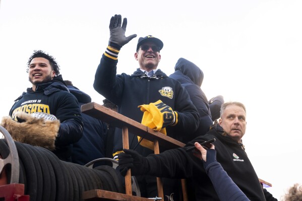 Michigan running back Blake Corum and coach Jim Harbaugh ride a firetruck during a parade celebrating Michigan's college football title, in Ann Arbor, Mich., Saturday, Jan. 13, 2024. (Jacob Hamilton/Ann Arbor News via AP)