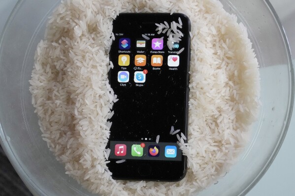 A view of a wet smartphone placed in a bowl of rice to dry, in London, Wednesday, Feb. 28, 2024. There's a lot of advice on the internet about what to do if you drop your phone in water, some of it conflicting. So what should you do then? Wipe as much moisture off as you can and leave it to dry. Don't use a hair dryer or put on a radiator. But whatever you do, don't dunk your device into a bowl of rice. (APPhoto/Frank Augstein)