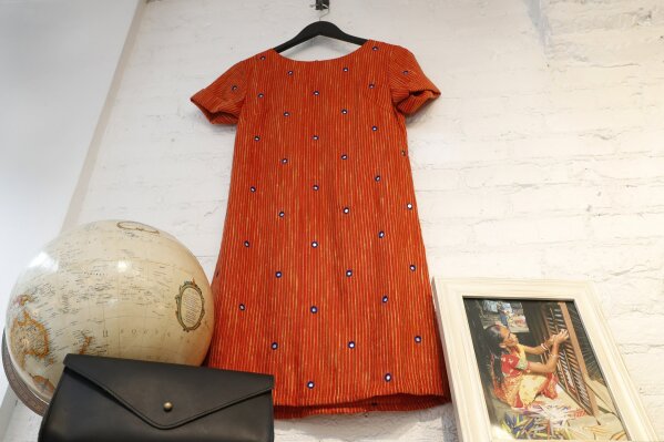 
              An orange Tikli shift dress with tiny mirrors embedded in the silk/cotton, handloom-blend fabric is displayed beside a photograph of an Indian woman weaving silk at Bhoomki, a store specializing in "ethically- fashioned" and hand-crafted clothing and jewelry, Tuesday, Jan. 23, 2018, in New York. Craftspeople in some of the poorest places on earth are making unexpected inroads into the U.S. retail market, expanding their clientele beyond museum shops and craft markets. (AP Photo/Kathy Willens)
            