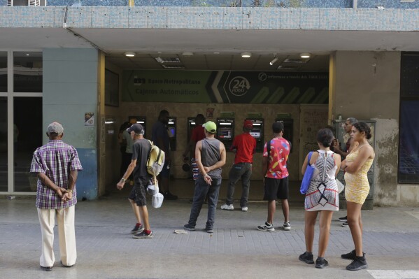 People stand in line outside a bank hoping to withdraw Cuban pesos from an ATM, in Havana, Cuba, Monday, April 22, 2024. An increasing number of Cubans are having to grapple with the country's shortage of cash. (AP Photo/Ariel Ley)