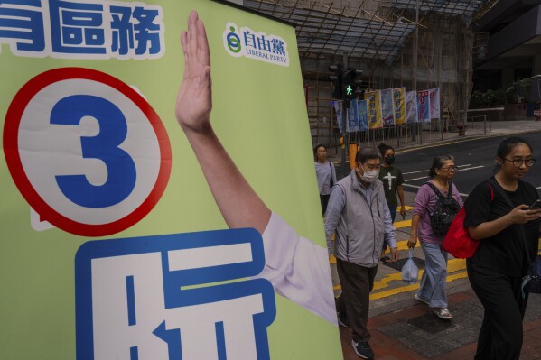 Pedestrians walk past a poster promoting a candidate during the District Council elections in Hong Kong, Sunday, Dec. 10, 2023. Residents went to the polls on Sunday in Hong Kong's first district council elections since an electoral overhaul was implemented under Beijing's guidance of “patriots” administering the city, effectively shutting out all pro-democracy candidates. (AP Photo/Louise Delmotte)