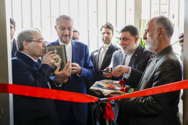 Syrian Foreign Minister Faisal Mekdad, left, kisses a copy of the Quran, the Islamic holy book, as he attends with Iranian Foreign Minister Hossein Amirabdollahian, second left, the opening ceremony of the new Iranian consulate building in Damascus, Syria, Monday, April 8, 2024. Iran's foreign minister Monday accused the United States of giving Israel the