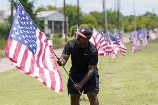 Bryan Smart plants American flags along Hillcroft Ave. as he walks toward The Fountain of Praise church Sunday, June 7, 2020, in Houston. A public memorial and private funeral service for George Floyd will be held at the church. Floyd died after being restrained by Minneapolis Police officers on Memorial Day. (AP Photo/David J. Phillip