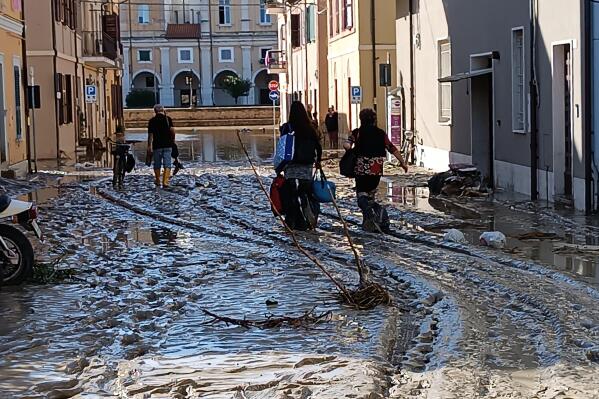 People walk on mud and debriS  in Senigallia, Italy, Friday Sept. 16, 2022. Floodwaters triggered by heavy rainfall swept through several towns in a hilly region of central-east Italy early Friday, leaving 10 people dead and several missing, state radio said. Dozens of survivors scrambled onto rooftops or up trees to await rescue. (Gabriele Moroni/LaPresse via AP)