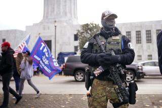 FILE - In this Nov. 7, 2020, file photo, a man holds a gun as he stands in front of the Oregon State Capitol building in Salem, Ore. Gov. Kate Brown on Tuesday, June 1, 2021, signed a bill that bans guns from the Oregon Capitol, changing a law that allowed concealed handgun licensees to bring firearms into the building. (AP Photo/Marcio Jose Sanchez, File)