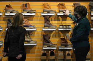 FILE - In this March 18, 2021 file photo, a salesperson helps a customer shopping for Bean Boots at the L.L. Bean flagship retail store  in Freeport, Maine.   Newly vaccinated and armed with $1,400 stimulus checks, Americans went on a spending spree last month, buying new clothes and going out to eat again. Retail sales surged a seasonally adjusted 9.8% after dropping about 3% the month before, the Commerce Department said Thursday, April 15. (AP Photo/Robert F. Bukaty, File)