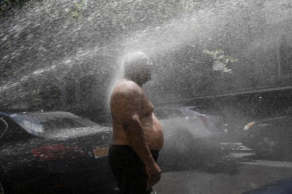 FILE - In this Tuesday, July 28, 2020 file photo, Rey Gomez cools off in the spray from a fire hydrant in New York, as the city opened more than 300 fire hydrants with sprinkler caps to help residents cool off during a heat wave. According to a study published Tuesday, May 25, 2021 in Nature Communications, during the summer of 2017 in nearly all large urban areas, people of color are exposed to more extreme urban heat than white people. (AP Photo/Mark Lennihan, File)