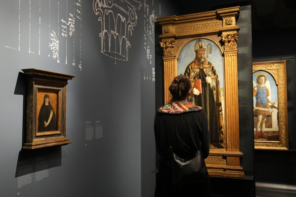 A visitor looks the Italian artist Piero della Francesca's paintings on the occasion of the inauguration of the exhibit "Piero della Francesca. Il Polittico Agostiniano riunito" (Piero della Francesca. The Augustinian Polyptych reunited) at Milan's Poldi Pezzoli museum, Italy, Tuesday, March 19, 2024. The Augustinian altarpiece originally comprised 30 sections in a polyptych, was dismantled after the Augustinians moved churches and eventually sold off. Only eight of the sections remain as individual paintings owned by museums in New York, Washington, D.C., London, Milan and Lisbon, Portugal. (AP Photo/Antonio Calanni)