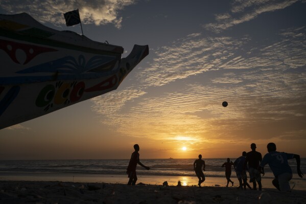 Silhouetted against the setting sun, youths play soccer next to a pirogue docked on the beach in Saint Louis, Senegal, Thursday, Jan. 19, 2023. (AP Photo/Leo Correa)