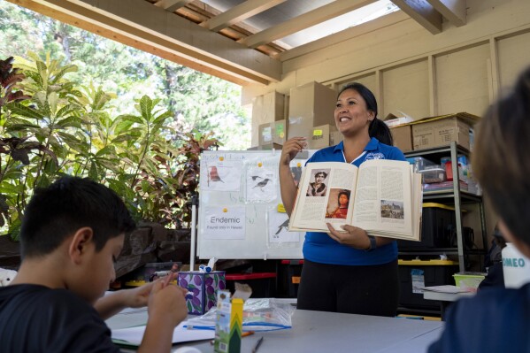 Sacred Hearts School teacher Charlene Ako shows a picture of the princess with a lei of bird feathers in connection with third graders from Princess Nāhiʻenaʻena Elementary at her class at Sacred Hearts Mission Church on Tuesday, Oct. 3, 2023, in Lahaina, Hawaii. Lahainaluna High, Lahaina Intermediate and Princess Nāhiʻenaʻena Elementary — have been closed for post-fire cleaning. (AP Photo/Mengshin Lin)