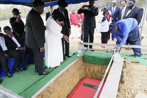 Bettersten Wade, center, watches as the body of her son, Dexter Wade, is lowered into a grave as she holds hands with civil rights attorney Ben Crump, right, in Jackson, Miss., Monday, Nov. 20, 2023. Dexter Wade, a 37-year-old man who died after being hit by a Jackson police SUV driven by an off-duty officer, was initially buried in a paupers cemetery without any notification to his family. (AP Photo/Rogelio V. Solis)