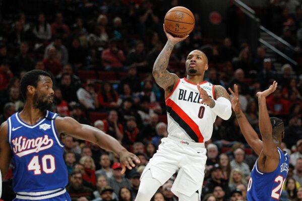 FILE - In this Saturday, March 7, 2020, file photo, Portland Trail Blazers guard Damian Lillard, center, shoots as Sacramento Kings forward Harrison Barnes, left, and forward Harry Giles III, right, defend during the first half of an NBA basketball game in Portland, Ore. Lillard says he will spend most of his downtime working on recording music while inside the NBA bubble. (AP Photo/Steve Dipaola, File)