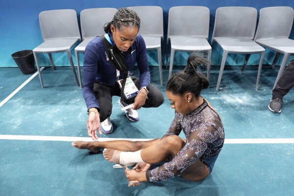 Simone Biles of United States, has her ankle taped after competing on the uneven bars during a women's artistic gymnastics qualification round at Bercy Arena at the 2024 Summer Olympics, Sunday, July 28, 2024, in Paris, France. (AP Photo/Charlie Riedel)