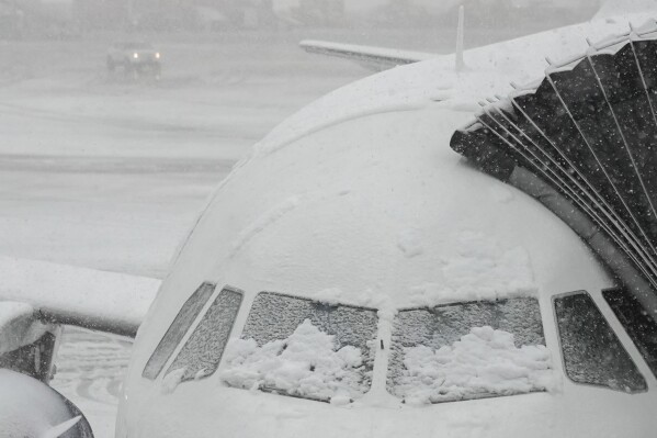 Snow covers the windows of a plane that sits at a gate at John F. Kennedy International Airport, Tuesday, Feb. 13, 2024, in New York. (AP Photo/Frank Franklin II)