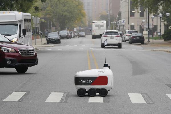 A food delivery robot crosses a street in Ann Arbor, Mich. on Thursday, Oct. 7, 2021. Robot food delivery is no longer the stuff of science fiction. Hundreds of little robots __ knee-high and able to hold around four large pizzas __ are now navigating college campuses and even some city sidewalks in the U.S., the U.K. and elsewhere. While robots were being tested in limited numbers before the coronavirus hit, the companies building them say pandemic-related labor shortages and a growing preference for contactless delivery have accelerated their deployment. (AP Photo/Carlos Osorio)