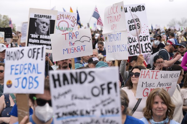 Demonstrators hold up signs during a "Hands Off!" protest against President Donald Trump at the Washington Monument in Washington, Saturday, April 5, 2025. (AP Photo/Jose Luis Magana)