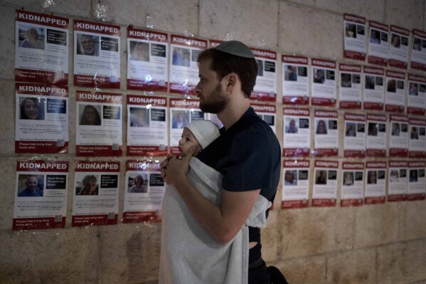 FILE - A man holds his baby as he looks at posters of the men, women and children held hostage by Hamas in the Gaza Strip, during a vigil marking 30 days since the Oct. 7 Hamas attack that started the fighting, in Jerusalem, Israel on Nov. 5, 2023. As the military sets its sights on southern Gaza in its campaign to stamp out Hamas, key challenges loom. International patience for a protracted invasion has begun to wear thin. And with some 2 million displaced Gaza residents staying in crowded shelters in the south in dire conditions, a broad military offensive there could unleash a new humanitarian disaster during the cold, wet winter. (AP Photo/Maya Alleruzzo, File)