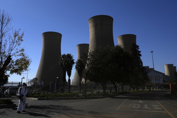 A worker blows leaves at the main entrance of the Komati Power Station in Middelburg, South Africa, Monday, June 19, 2023. The coal-fired plant was shut down to make way for a solar, wind and battery storage plant. (AP Photo/Themba Hadebe)