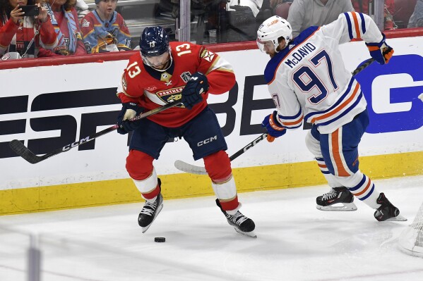 Florida Panthers center Sam Reinhart (13) and Edmonton Oilers center Connor McDavid (97) go for the puck during the first period of Game 1 of the NHL hockey Stanley Cup Finals, Saturday, June 8, 2024, in Sunrise, Fla. (AP Photo/Michael Laughlin)