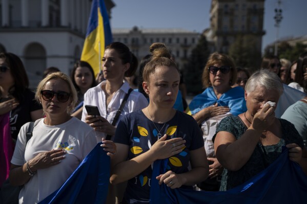 Women cry while listening to the Ukrainian national anthem at a protest calling for the release of Ukrainian soldiers captured by Russians at the Independence Square in Kyiv, Ukraine, Sunday, Aug. 27, 2023. The protest marks five hundred days since the soldiers were captured in the besieged city of Mariupol. (AP Photo/Bram Janssen)