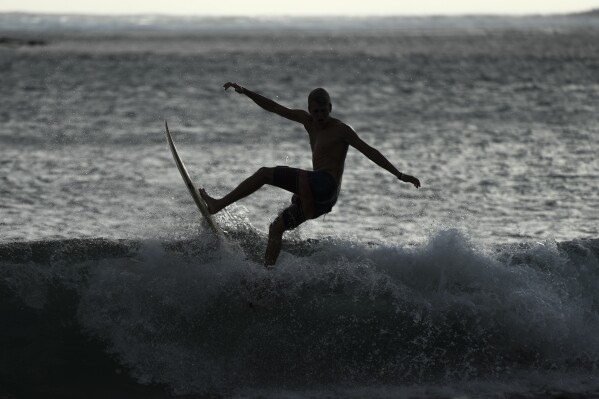 A silhouette of a surfer is seen in Te Aupoo, Tahiti, French Polynesia, Sunday, January 14, 2024.  (AP Photo/Daniel Cole)