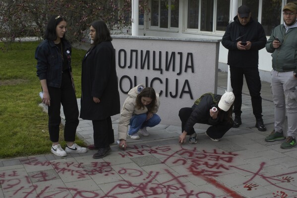 Люди используют красную аэрозольную краску перед местным полицейским участком во время антикоррупционной акции протеста под руководством студентов университета в юго-западном городе Нови-Пазар, Сербия, в субботу, 12 апреля 2025 года. (AP Photo/Марко Дробнякович)