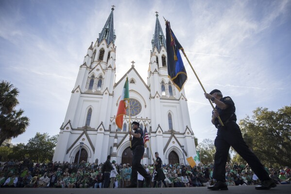 FILE - Participants carry flags past the Cathedral Basilica of St. John the Baptist while marching in the St. Patrick's Day parade, March 17, 2023, in historic downtown Savannah, Ga. Savannah, Georgia's oldest city, is planning a supersized celebration as it marks the 200th anniversary of its beloved St. Patrick's Day parade. City Manager Jay Melder says he's expecting historic crowds for the Irish-themed parade Saturday, March 16, 2024. (AP Photo/Stephen B. Morton)