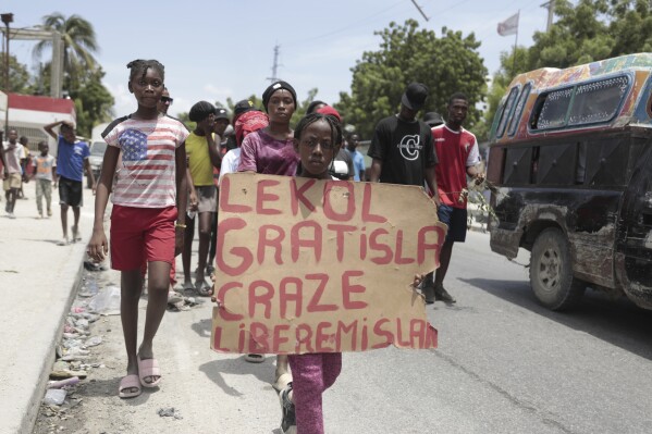 A girl carries a sign that reads in Creole 