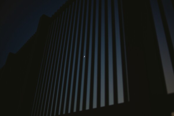 The moon is seen behind the border wall in Eagle Pass, Texas, on Friday evening, Aug. 9, 2024. (Jordan Vonderhaar/The Texas Tribune via AP)