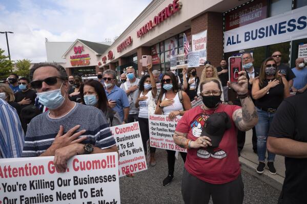 A crowd gives the Pledge of Allegiance while supporting Bobby Catone, the owner of a Staten Island tanning salon, Thursday, May 28, 2020, in New York. Catone opened the salon briefly Thursday morning in defiance of a law requiring non-essential businesses to remain closed during the coronavirus pandemic. (AP Photo/Mark Lennihan)