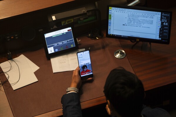 A lawmaker watches his phone during the second reading of the Basic Law Article 23 legislation at the Legislative Council in Hong Kong, Tuesday, March 19, 2024. (AP Photo/Louise Delmotte)