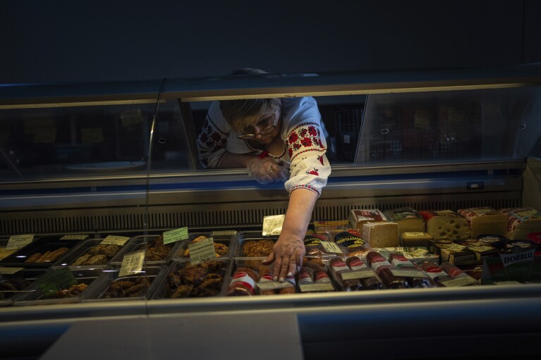 A saleswoman places goods in a refrigerator in a store that runs on a generator after the municipality temporarily cut the power to conserve energy in Kharkiv, Ukraine, on Sunday, April 14, 2024. (AP Photo/Evgeniy Maloletka)