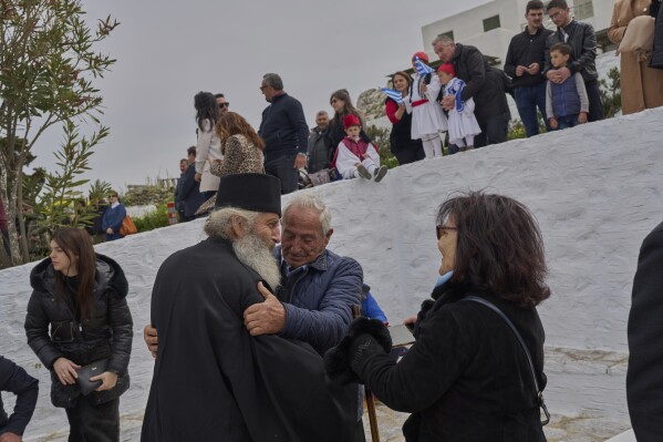 O monge cristão ortodoxo Padre Spyridon é abraçado pelos moradores da ilha enquanto as pessoas se reúnem para assistir a um desfile no Dia da Independência da Grécia, que comemora o início da Guerra da Independência Grega em 1821, na ilha de Amorgos, Grécia, na terça-feira, 25 de março de 2025. (Foto AP/Petros Giannakouris)