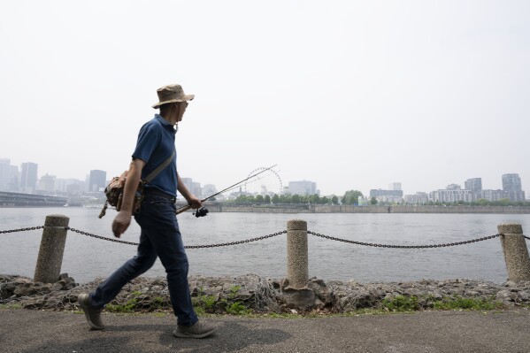 A man walks along the St. Lawrence River in front of the Old Port of Montreal on Friday, June 6, 2025. Smoke from the wildfires in the Canadian Prairies is causing poor air quality and reduced visibility in the Greater Montreal region. (Christinne Muschi /The Canadian Press via AP)