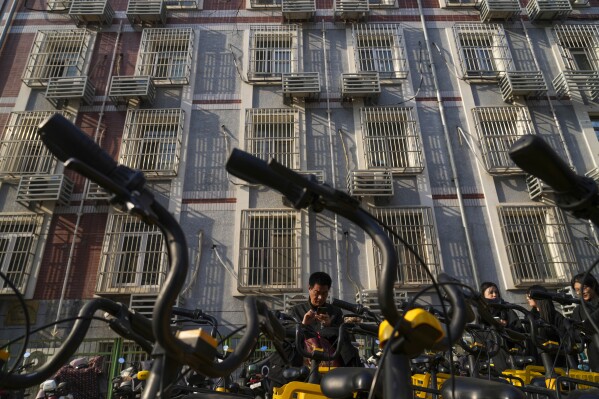 A man uses his phone to unlock a rental bike in front of an apartment in Beijing, China, Friday, April 5, 2024. (AP Photo/Tatan Syuflana)