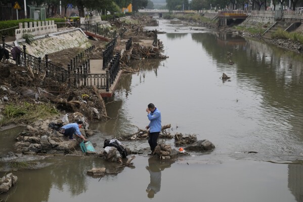 Residents wash their suitcase and belongings on a damaged bank of a canal clogged with flood debris in the aftermath of flood waters from an overflowing river in the Mentougou district on the outskirts of Beijing on Monday, Aug. 7, 2023. The death toll in recent flooding in China's capital rose, officials said Wednesday, as much of the country's north remains threatened by unusually heavy rainfall. (AP Photo/Andy Wong)