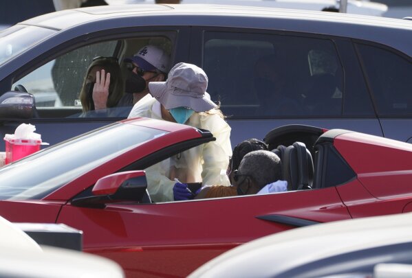 A woman is vaccinated inside a convertible vehicle at a mass COVID-19 vaccination site outside The Forum in Inglewood, Calif., Tuesday, Jan. 19, 2021. California has become the first state to record more than 3 million known coronavirus infections. That's according to a tally Monday by Johns Hopkins University.  (AP Photo/Damian Dovarganes)