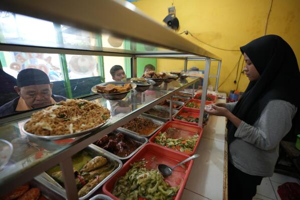 A worker serves customers at a food stall in Bekasi, on the outskirts of Jakarta, Indonesia, Thursday, Feb 2, 2023. Nearly a year after Russia invaded Ukraine, punishingly high food prices are inflicting particular hardship on the world’s poor. In Jakarta, vendors know they can’t pass along surging food prices to their already struggling customers. (AP Photo/Achmad Ibrahim)